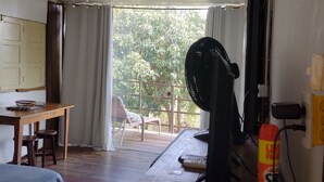 A room with a bed, a wooden table with two stools, a fan, and a window with curtains. - Palhoça da Colina (Fernando de Noronha)