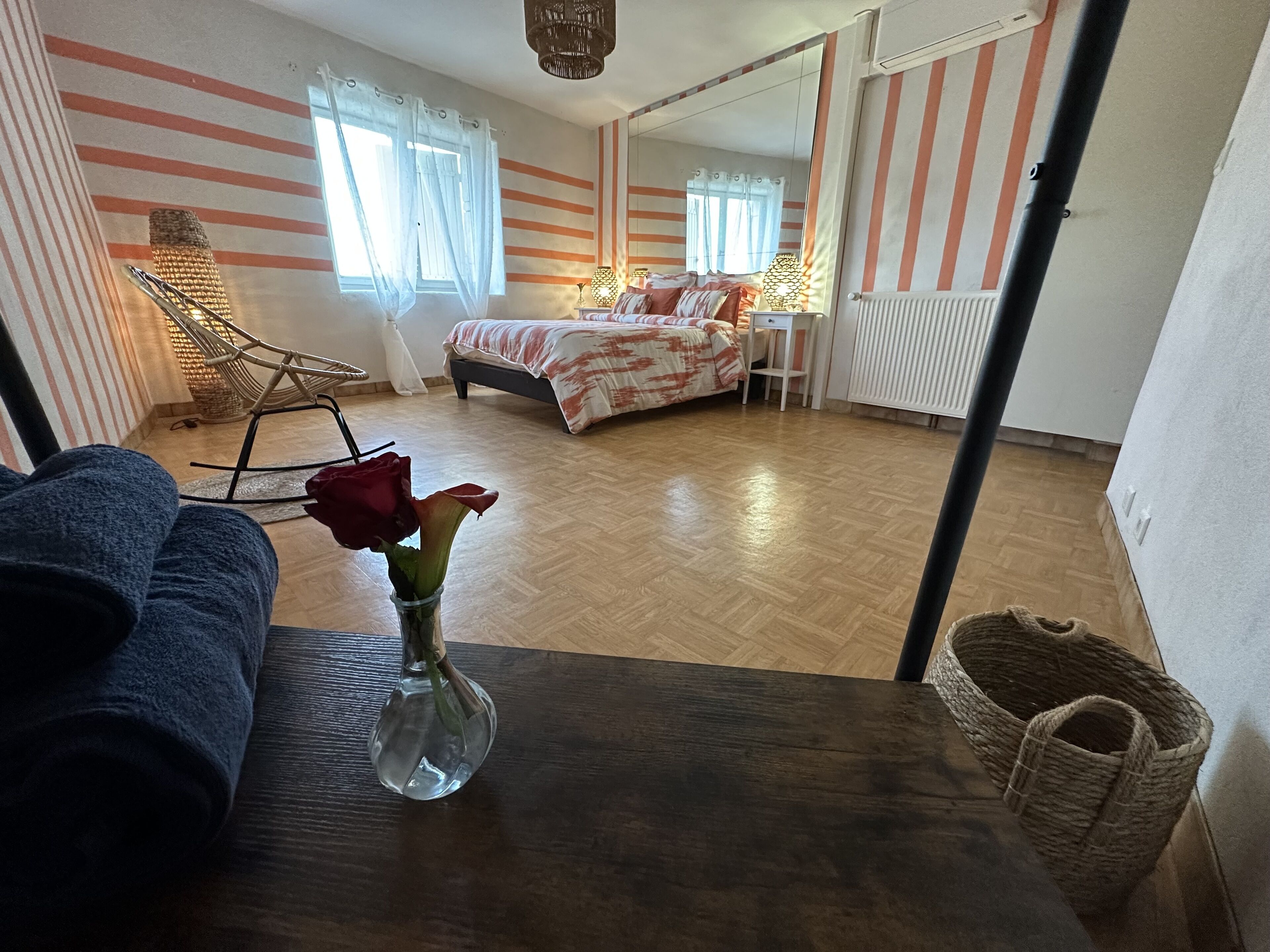 A room with a bed, a chair, a table, and a vase with flowers.