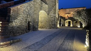 A stone building with a tower, a courtyard with a paved path, and a building with arches in the background. - Logement Paisible - Mas Sogusthenna (Mons)
