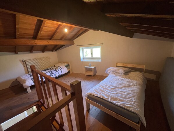 Un dormitorio con zona de descanso elevada, una mesita de noche pequeña, una ventana y una silla de madera.