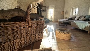 A rustic interior with a large woven basket, a woven pouf, a sofa, and a wall clock. - Logement Paisible - Mas Sogusthenna (Mons)