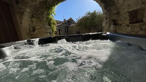 A hot tub with water bubbling, surrounded by stone walls and an archway. - Logement Paisible - Mas Sogusthenna (Mons)