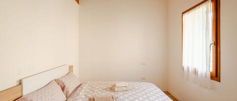 A bedroom with a bed, a wooden headboard, a window with curtains, and a ceiling with exposed beams.
