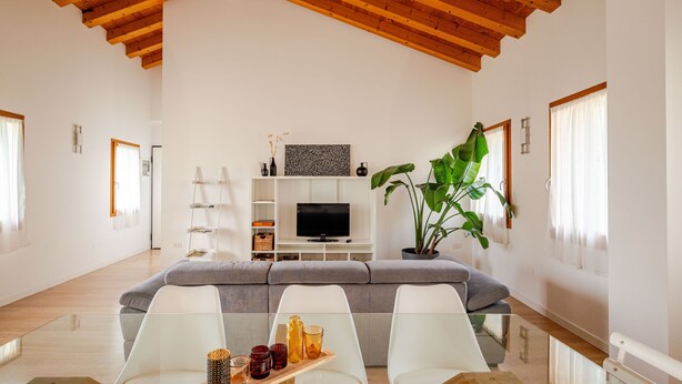 A modern living room with a high ceiling, a grey sofa, white chairs, a wooden coffee table, and a large green plant. - Ca Mantoet Valdobbiadene - 3Bedroom Loft (Valdobbiadene)