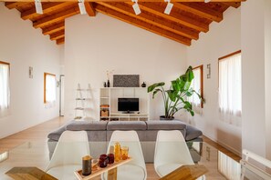 A modern living room with a high ceiling, a grey sofa, white chairs, a wooden coffee table, and a large green plant. - Ca Mantoet Valdobbiadene - 3Bedroom Loft (Valdobbiadene)