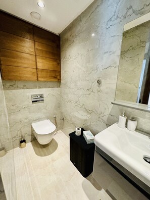 Ein modernes Badezimmer mit Marmorwand, Holzschränken, einer weißen Toilette, einem schwarzen Waschtisch und einem großen Spiegel.