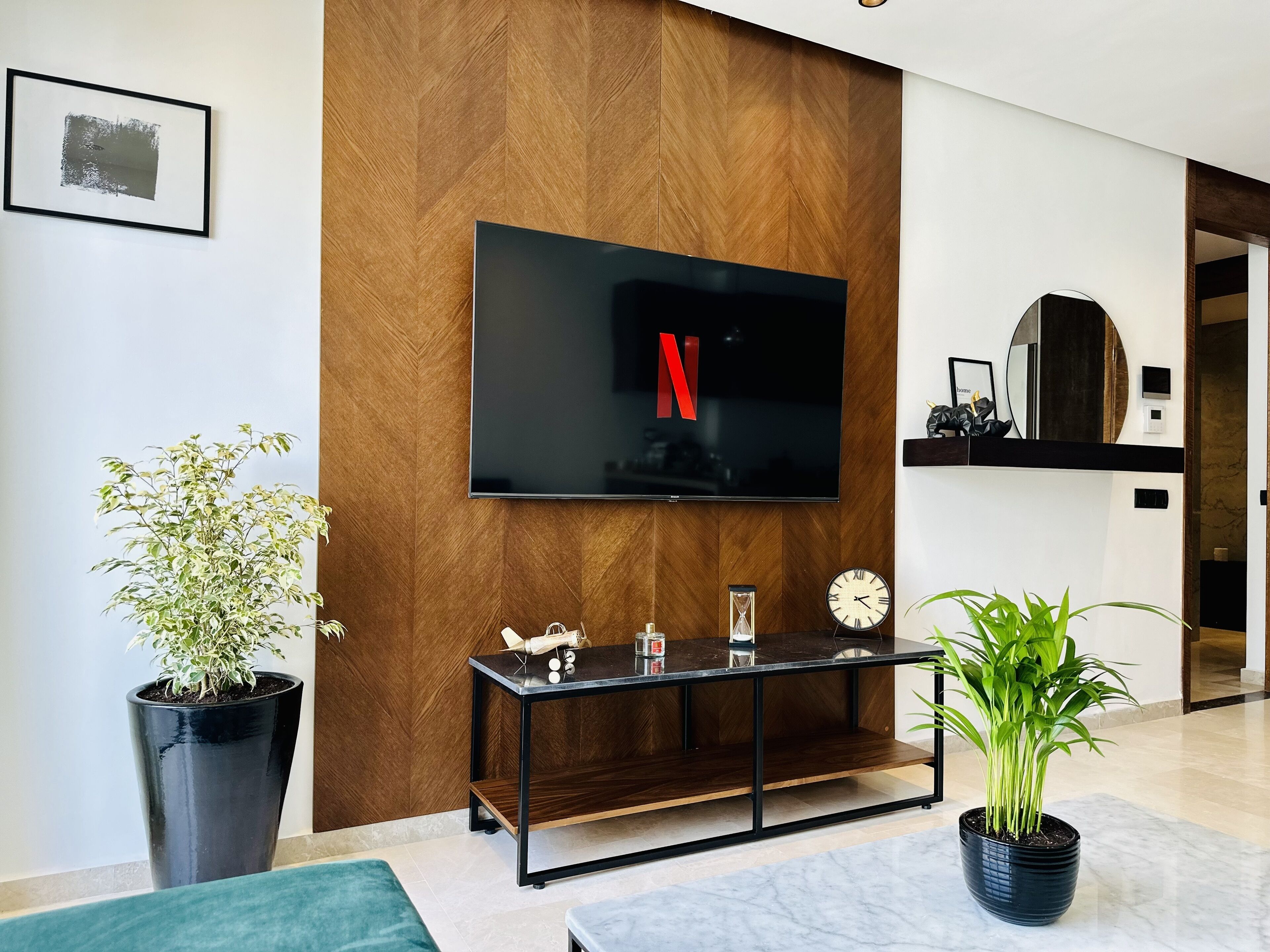 Una sala de estar moderna con un televisor de pantalla plana montado en una pared de madera, una mesa de centro con objetos decorativos y plantas en macetas.