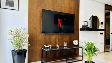 Una sala de estar moderna con un televisor de pantalla plana montado en una pared de madera, una mesa de centro con objetos decorativos y plantas en macetas.