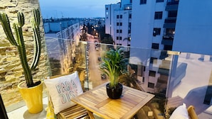 A balcony with a wooden table and chairs, potted plants, and a view of the cityscape. - Stay'Inn - Stadium Penthouse (Casablanca)