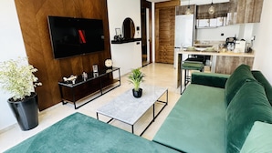 A modern living room with a large green sofa, a flat-screen TV, a coffee table, and a potted plant. - Stay'Inn - Stadium Penthouse (Casablanca)