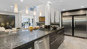 Een moderne keuken met granieten aanrechtbladen, roestvrijstalen apparatuur, hanglampen en een groot eiland.