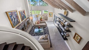 Een ruime woonkamer met een hoge plafond, een trap en uitzicht op de omgeving.