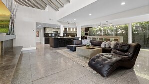 Een ruime woonkamer met een moderne keuken, een leren bank en een eethoek met een groot raam.