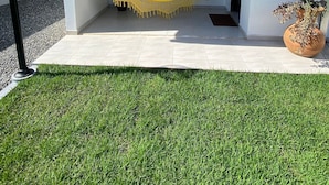 A covered outdoor seating area with a hammock, a potted plant, and a wall-mounted light fixture.