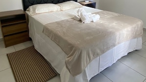 A neatly made bed with a headboard, a bedside table with a lamp, and a small wooden nightstand.