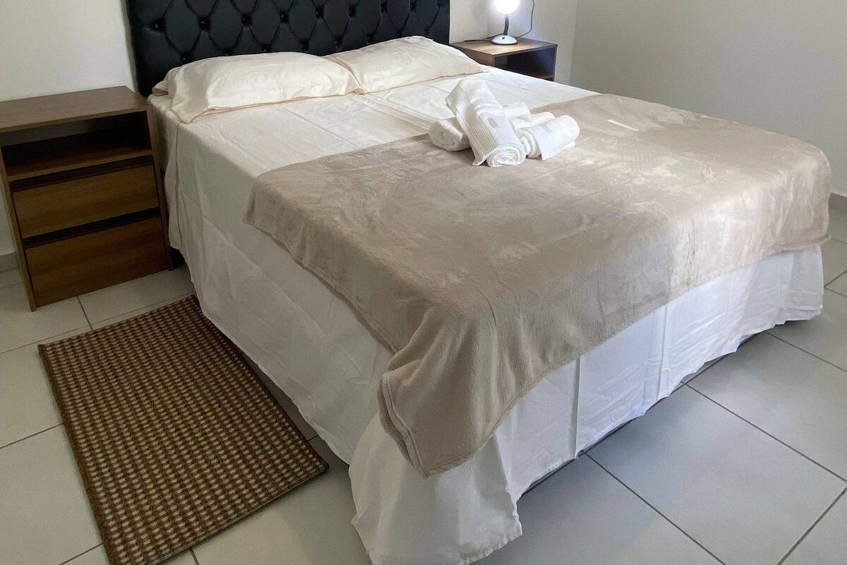 A neatly made bed with a headboard, a bedside table with a lamp, and a small wooden nightstand.