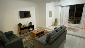 A modern living room with a grey sofa, a wooden coffee table, and a flat-screen TV mounted on the wall.