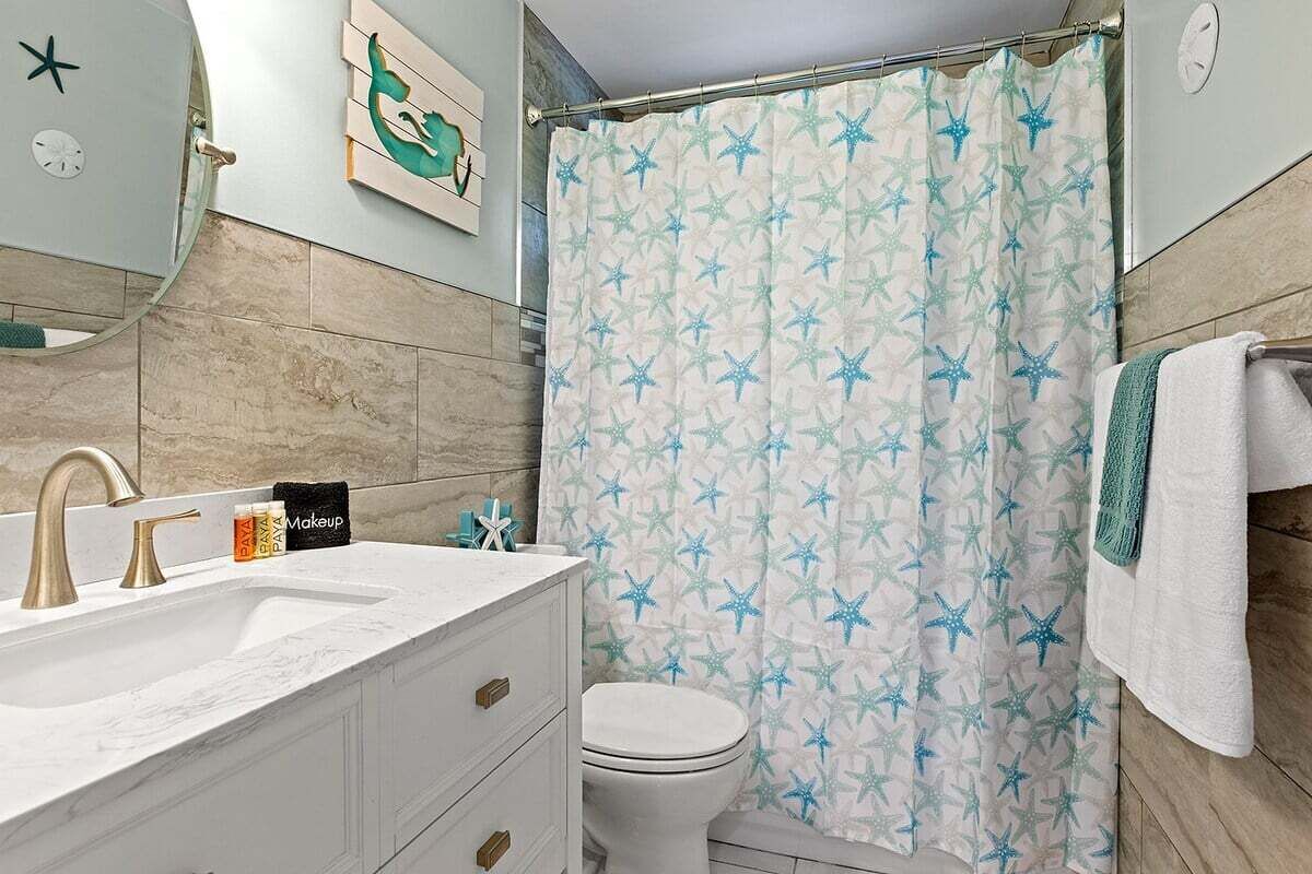 A bathroom with a white sink, gold faucets, a white toilet, and a shower curtain with star patterns.