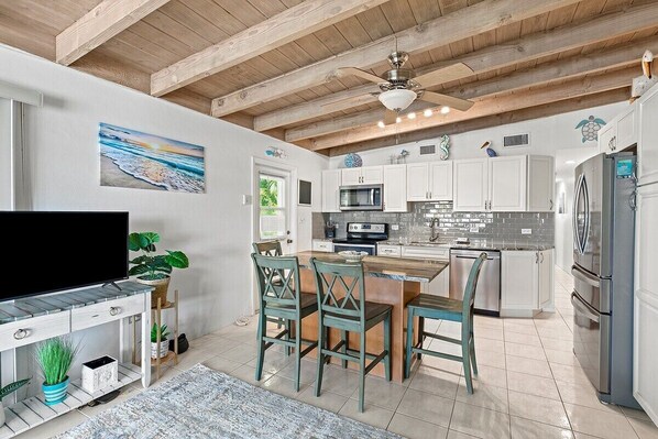 A modern kitchen with white cabinets, a wooden ceiling, and a dining area with teal chairs.