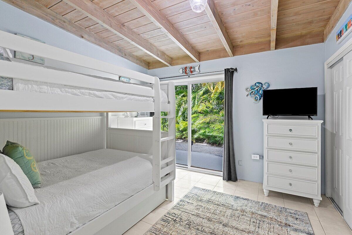 Een slaapkamer met een stapelbed, een dressoir, een televisie en een schuifdeur naar een balkon.