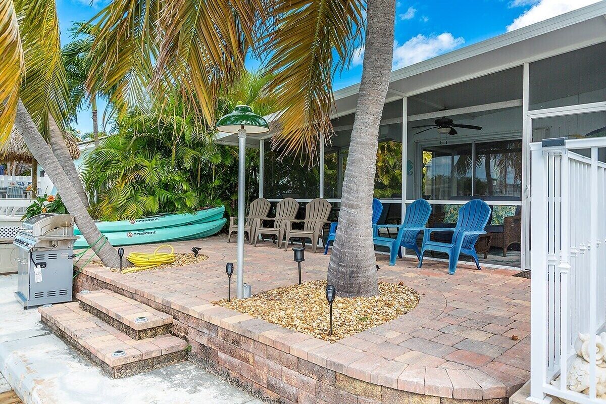 A covered outdoor patio with steps leading to a seating area, surrounded by palm trees and a boat.