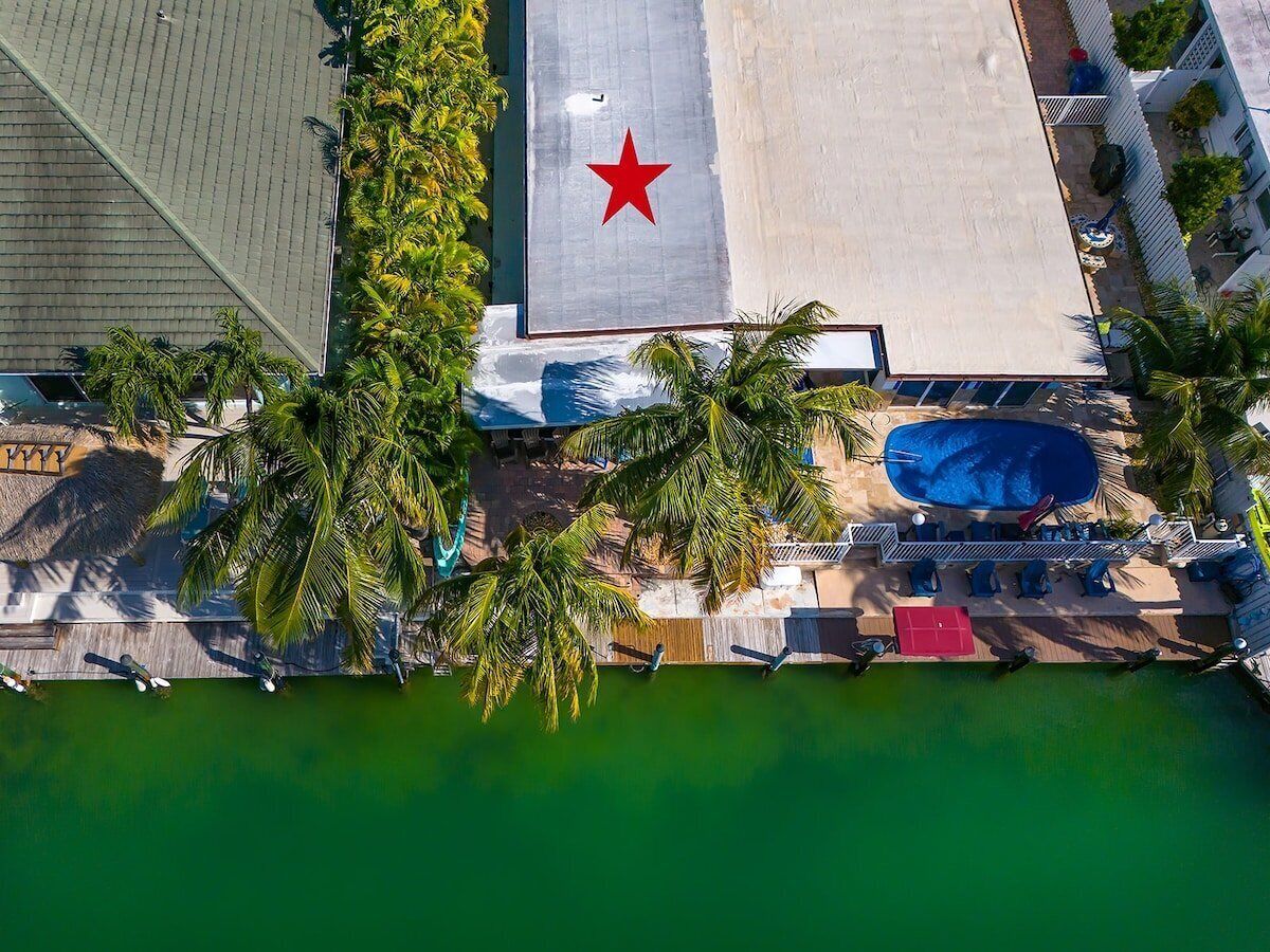 An aerial view of a resort with a swimming pool, palm trees, and a large building with a red star.