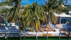 Una propiedad frente al mar con muelle, sillas de descanso, piscina y palmeras.