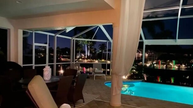 Zona de piscina con vistas a la ciudad de noche, mobiliario exterior y un patio cubierto.