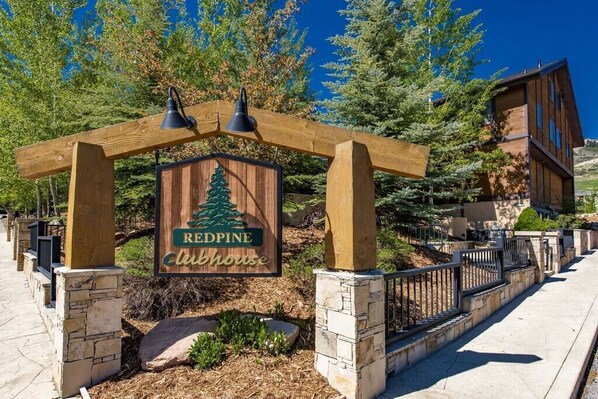 A wooden sign with a pine tree and the words "Redpine Clubhouse" under a wooden pergola.