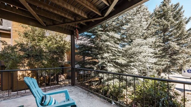 A balcony with blue chairs and a view of snow-covered trees.