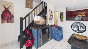 A modern living room with a staircase, a flat-screen TV, a red abstract sculpture, a blue patterned sofa, and a decorative wall piece. - La Tranche-sur-Mer, house for 3 adults / 2 children (La Tranche-sur-Mer)