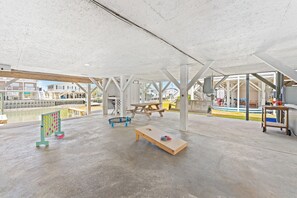 Un espace de loisirs intérieur doté d’un sol en béton, de bancs en bois, d’un trampoline et d’une table de billard.