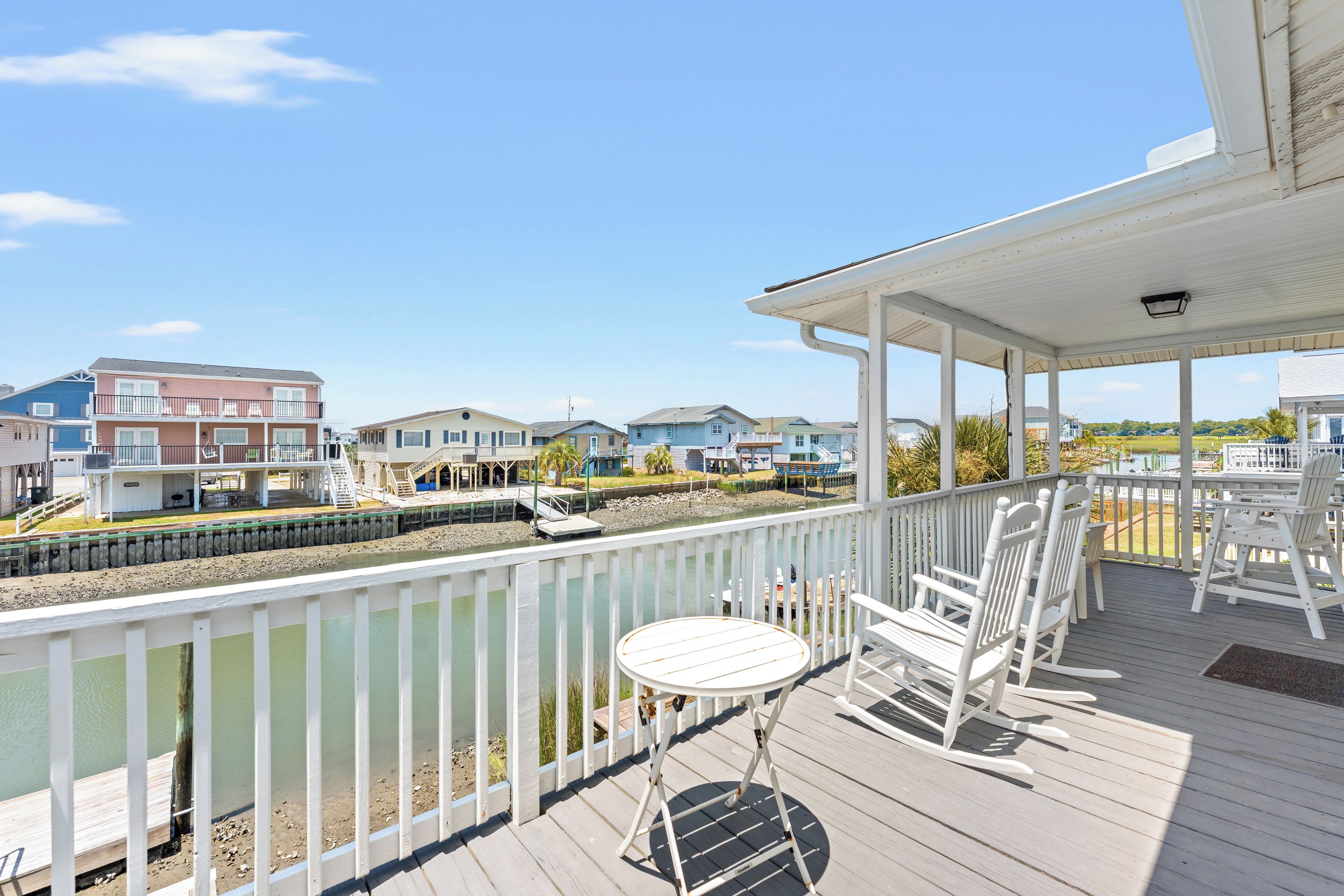 A wooden deck with a table and chairs, overlooking a water body and residential buildings.