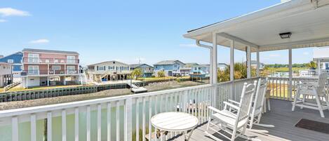 A wooden deck with a table and chairs, overlooking a water body and residential buildings.