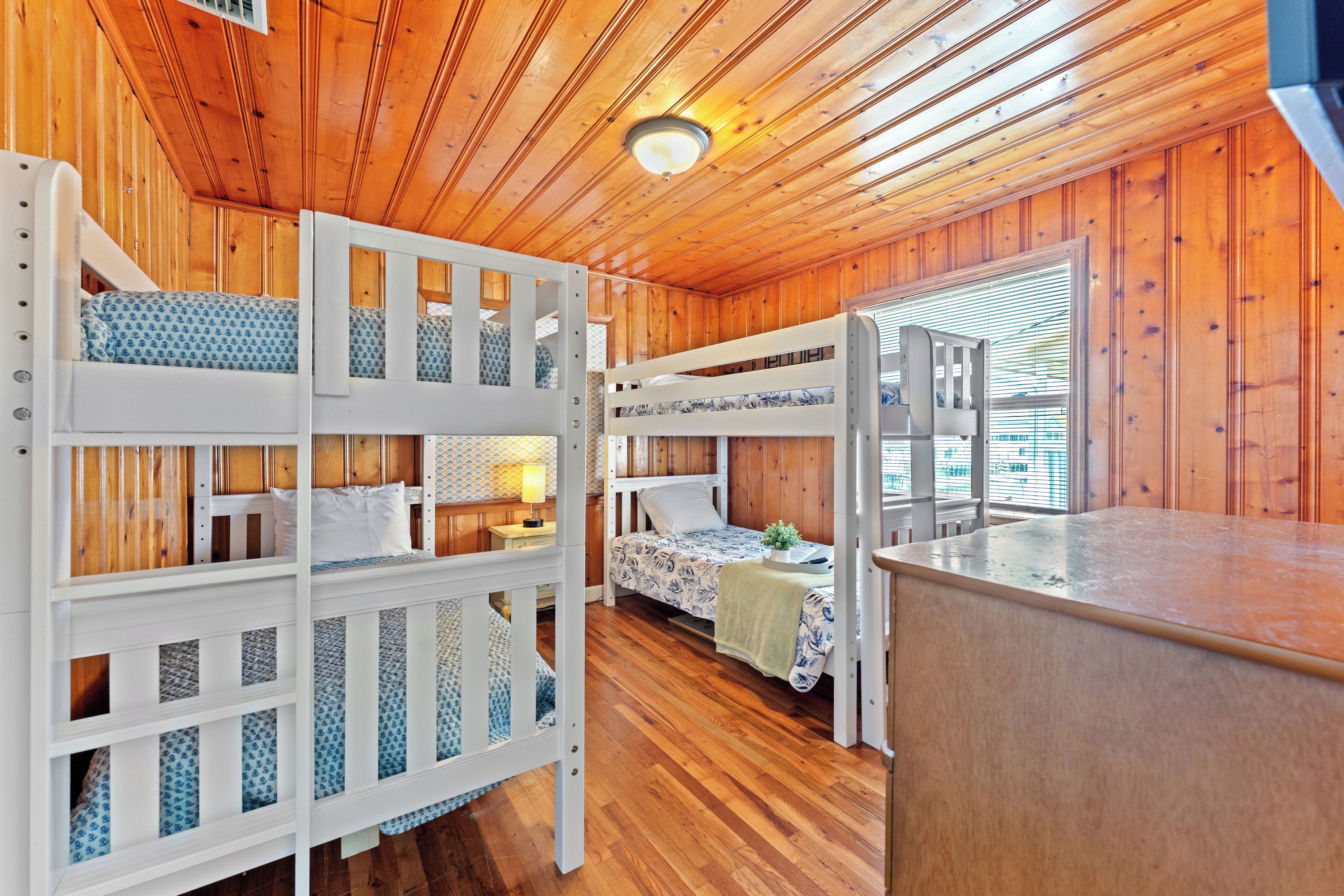 Ein Holzhütten-Interieur mit Etagenbetten, Holzwänden, einer Küchenzeile und einem Fenster mit Jalousien.