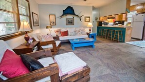 A cozy living room with a sofa, a coffee table, and a dining area with stools. - Hasell Cottage, Oceanside House in Emerald Isle, NC! (Emerald Isle)