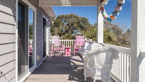Une véranda couverte avec une balustrade blanche, deux chaises roses et un fauteuil en osier.