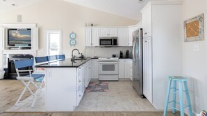 Une cuisine moderne avec des meubles blancs, un îlot central, un four à micro-ondes, un réfrigérateur et un téléviseur placé au-dessus de l’îlot.