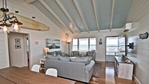 Amplio salón con un sofá grande de color gris, una mesa de comedor de madera y vistas al océano a través de amplias ventanas.