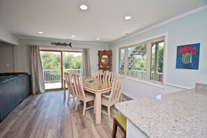 A modern kitchen with a dining area, large windows, and a balcony with a view of trees. - Hollandaise, Oceanview House in Emerald Isle, NC! (Emerald Isle)