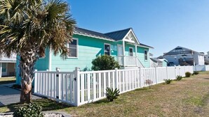 Une maison turquoise avec une clôture blanche en bois, un palmier et un ciel bleu azur.