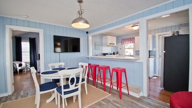 Un espace repas avec une table ronde, des chaises blanches et des tabourets de bar rouges.