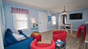 Un salon avec un canapé bleu, des fauteuils rouges, une petite table et un téléviseur fixé au mur.