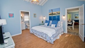 Une chambre à coucher avec un lit, un ventilateur de plafond, un tableau et une porte donnant sur une autre pièce.