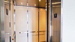 An elevator interior with metallic walls, a glass door, and a floor with a patterned tile design. - Island Beach Racquet Club 105B, Oceanside Condo in Atlantic Beach, NC! (Atlantic Beach)