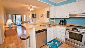 A compact kitchen with white cabinets, a dishwasher, a stove, and a coffee maker. - Island Beach Racquet Club 105B, Oceanside Condo in Atlantic Beach, NC! (Atlantic Beach)