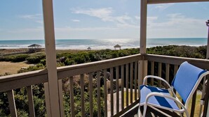 A balcony with a view of the beach, two chairs, and a small structure in the distance. - Island Beach Racquet Club 303A, Oceanfront Condo in Atlantic Beach, NC! (Atlantic Beach)