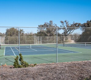 A tennis court enclosed by a chain-link fence with trees in the background. - Island Beach Racquet Club 303A, Oceanfront Condo in Atlantic Beach, NC! (Atlantic Beach)