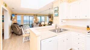 A modern kitchen with white cabinets, a dishwasher, and a large window overlooking the sea. - Island Beach Racquet Club 303A, Oceanfront Condo in Atlantic Beach, NC! (Atlantic Beach)