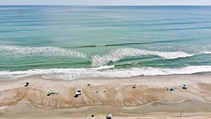 Une plage avec des gens et des parasols, un ciel dégagé et des vagues douces.